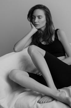 A contemplative woman in black attire sitting indoors, captured in black and white.