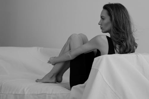 Back View of a Woman in a Black Dress Sitting on the Bed