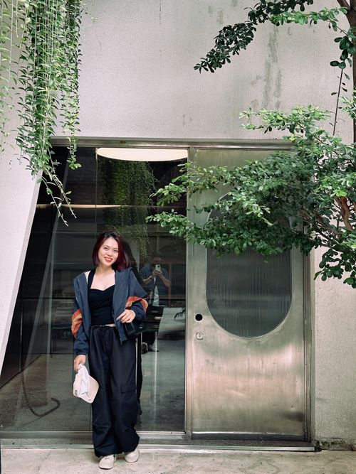 Free A fashionable woman smiling in an urban setting with greenery, showcasing modern lifestyle. Stock Photo