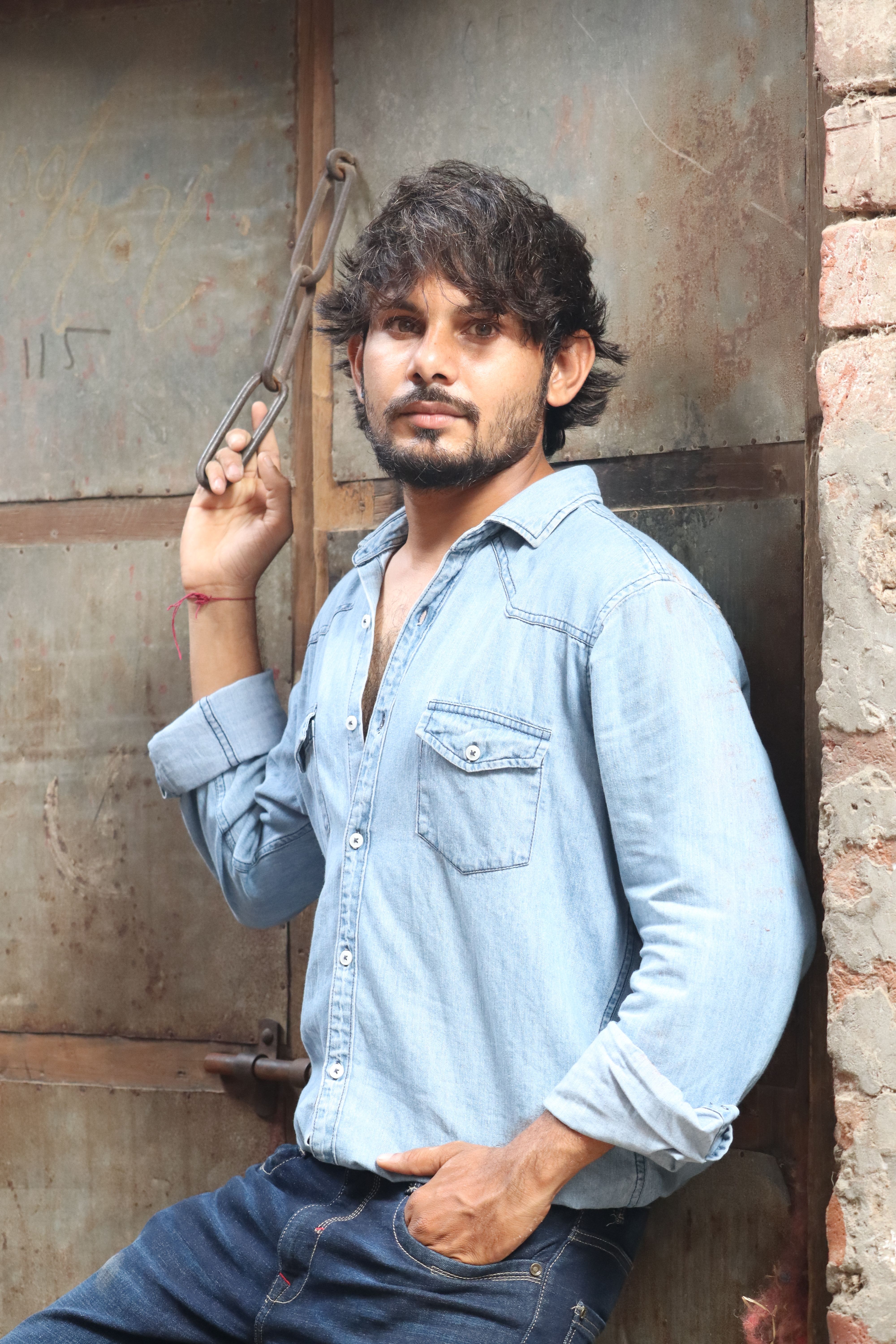 Fashionable young man posing outdoors in an industrial area wearing a denim shirt in Ahmedabad, India.