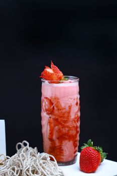 Delicious strawberry smoothie in a tall glass garnished with fresh mint and whole strawberries.