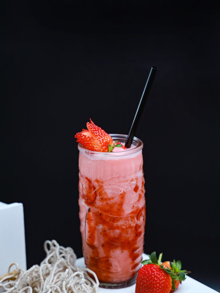 A strawberry smoothie in a tall glass against a black background