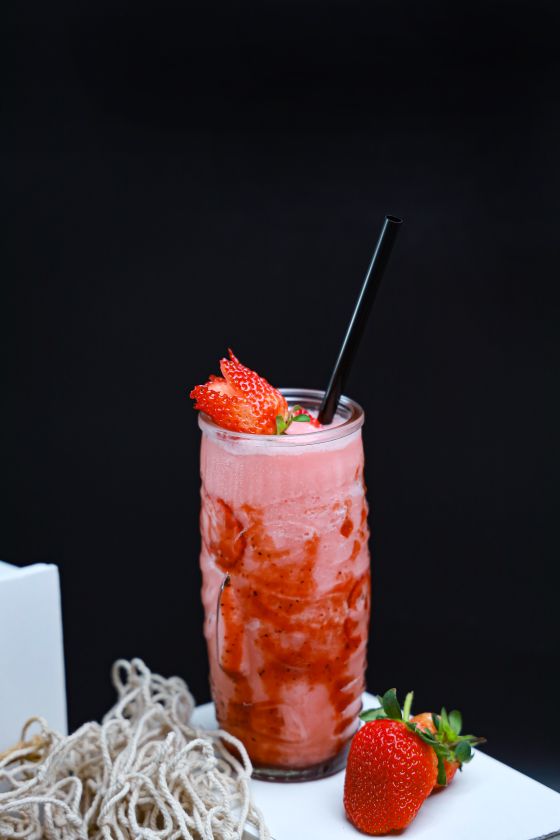 Pink strawberry smoothie streaked with strawberry sauce in a tall glass with a black straw