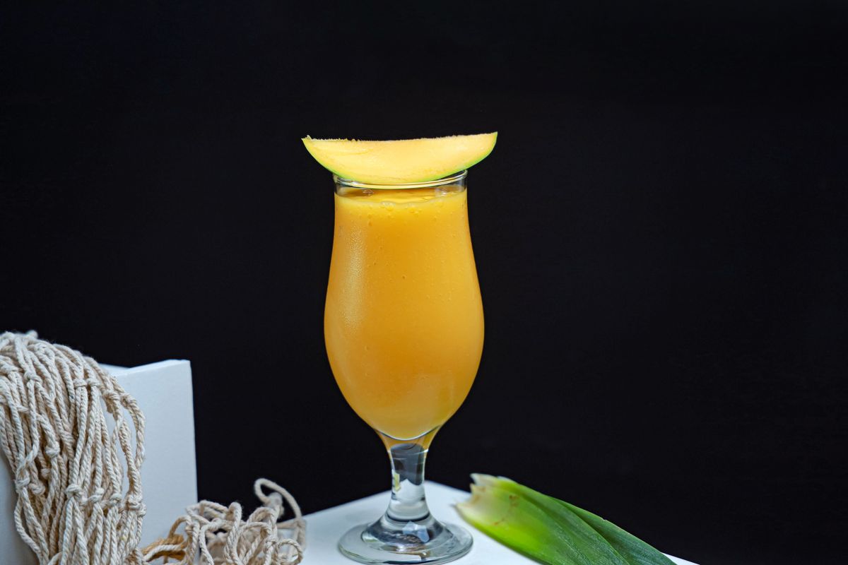 Thick orange mango smoothie in a hurricane glass topped with a fresh mango slice