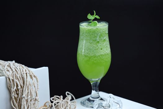 A fresh and healthy green smoothie in a glass with a mint garnish, placed against a dark background.