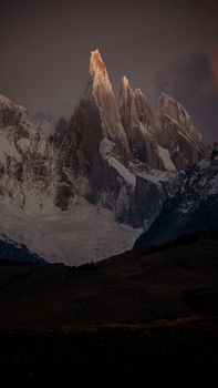 Majestic mountain peaks capped with snow under a dramatic sunset sky, showcasing natural beauty.