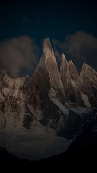 Snow-covered jagged mountain peaks with rugged terrain under moody twilight skies.