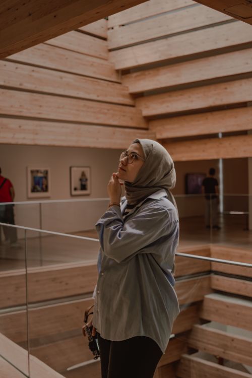 Free Woman in headscarf exploring a modern art gallery with wooden architecture. Stock Photo