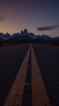 Empty highway leading to mountains at dusk, showcasing a stunning sunset view.