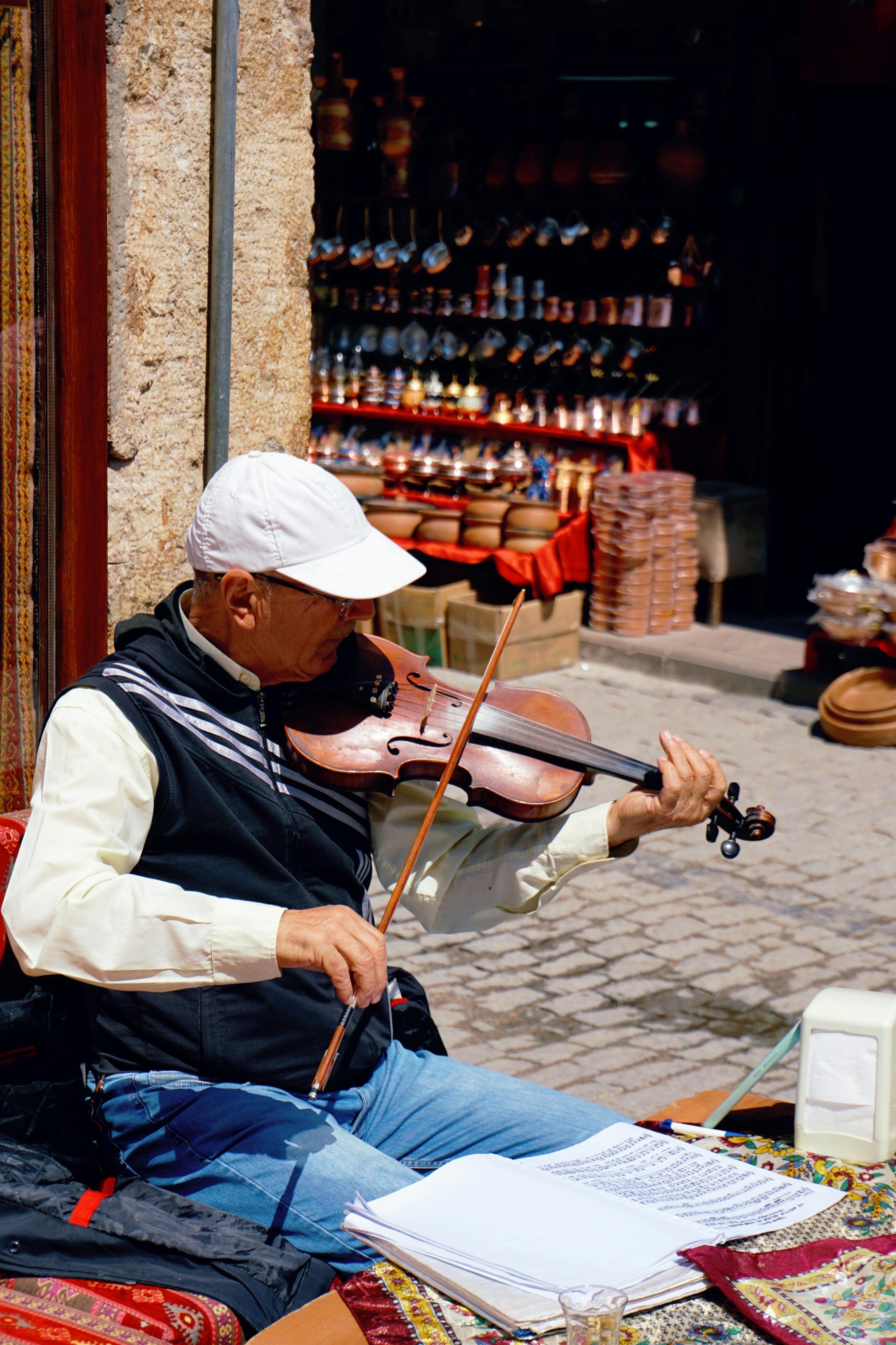 Elderly man playing violin on a sunny day in an urban market, adding charm to the lively street scene.