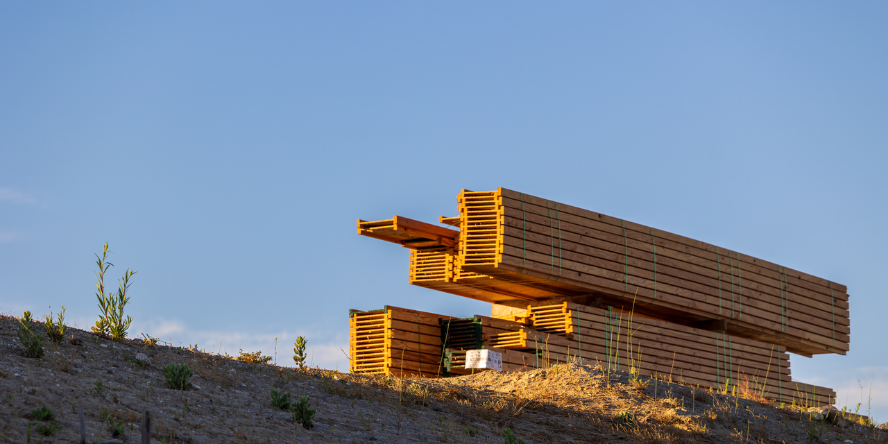 Stacked wooden trusses at a construction site in bright sunlight, highlighting natural wood textures.