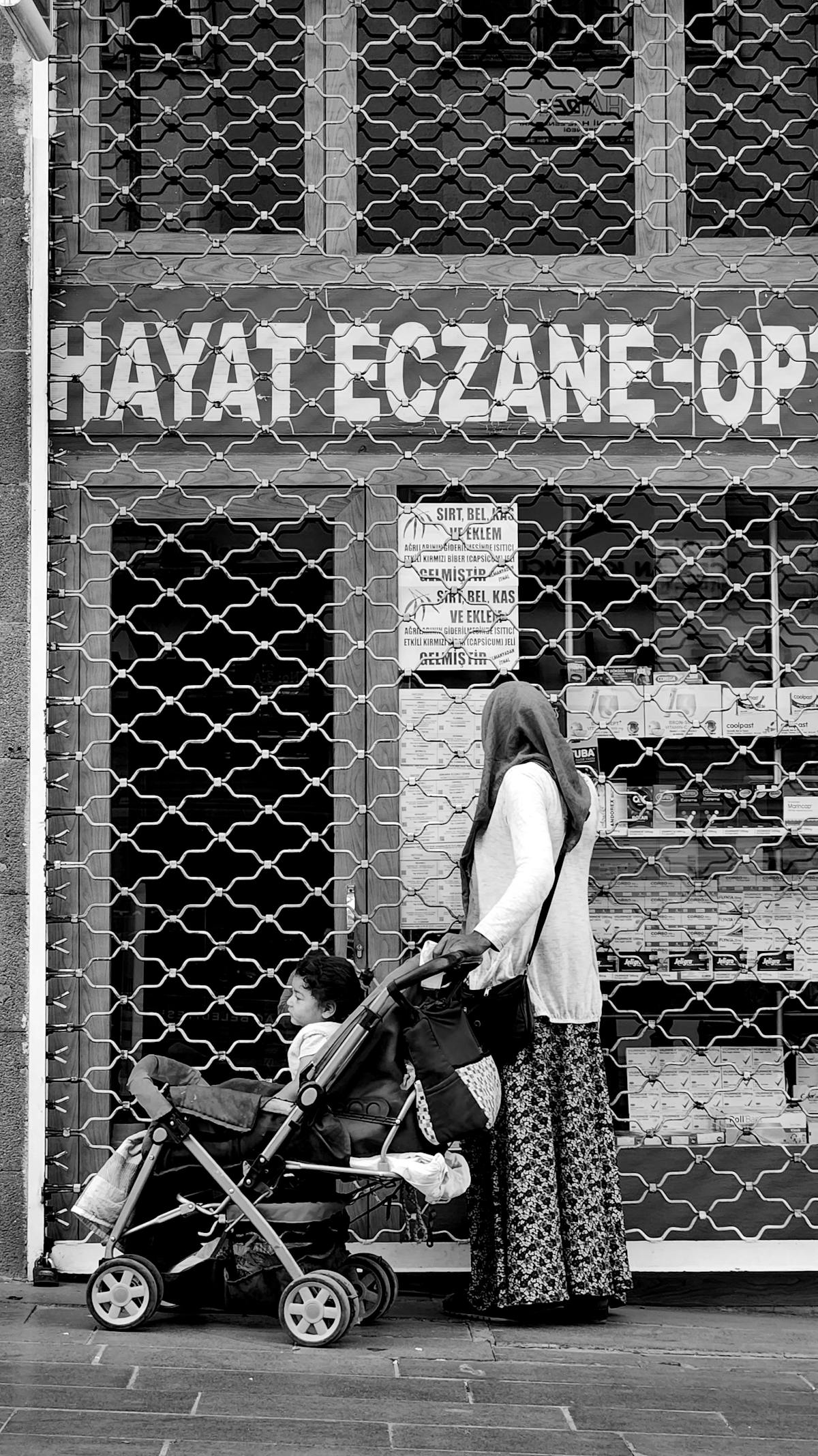 Donna con bambino nel passeggino fermo davanti a una farmacia affollata