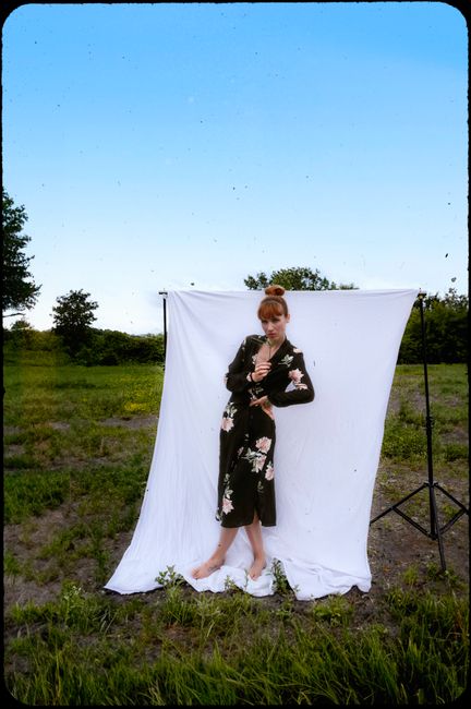 Woman in a floral dress against a white backdrop outdoors, blending nature with fashion.