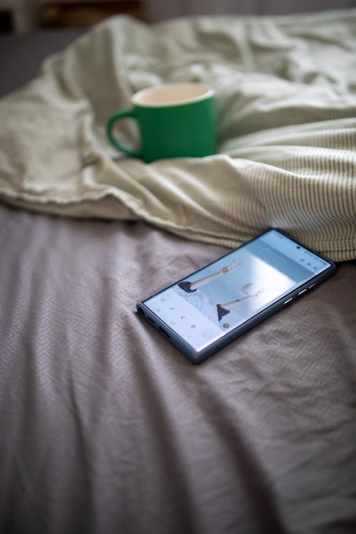 Smart Phone and Coffee Cup Lying on a Bed