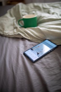 Smartphone and coffee mug on bed in cozy bedroom setting.