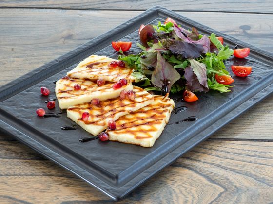 Grilled halloumi slices with pomegranate seeds, balsamic drizzle and mixed leaf salad on slate