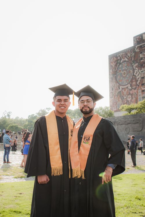 Free Graduates posing with academic gowns in front of UNAM library mural in Mexico City. Stock Photo