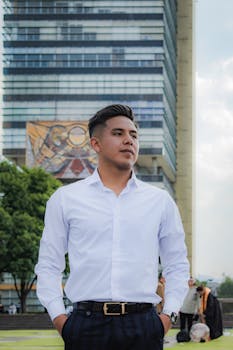 Young man in white shirt poses confidently against modern urban architecture backdrop.