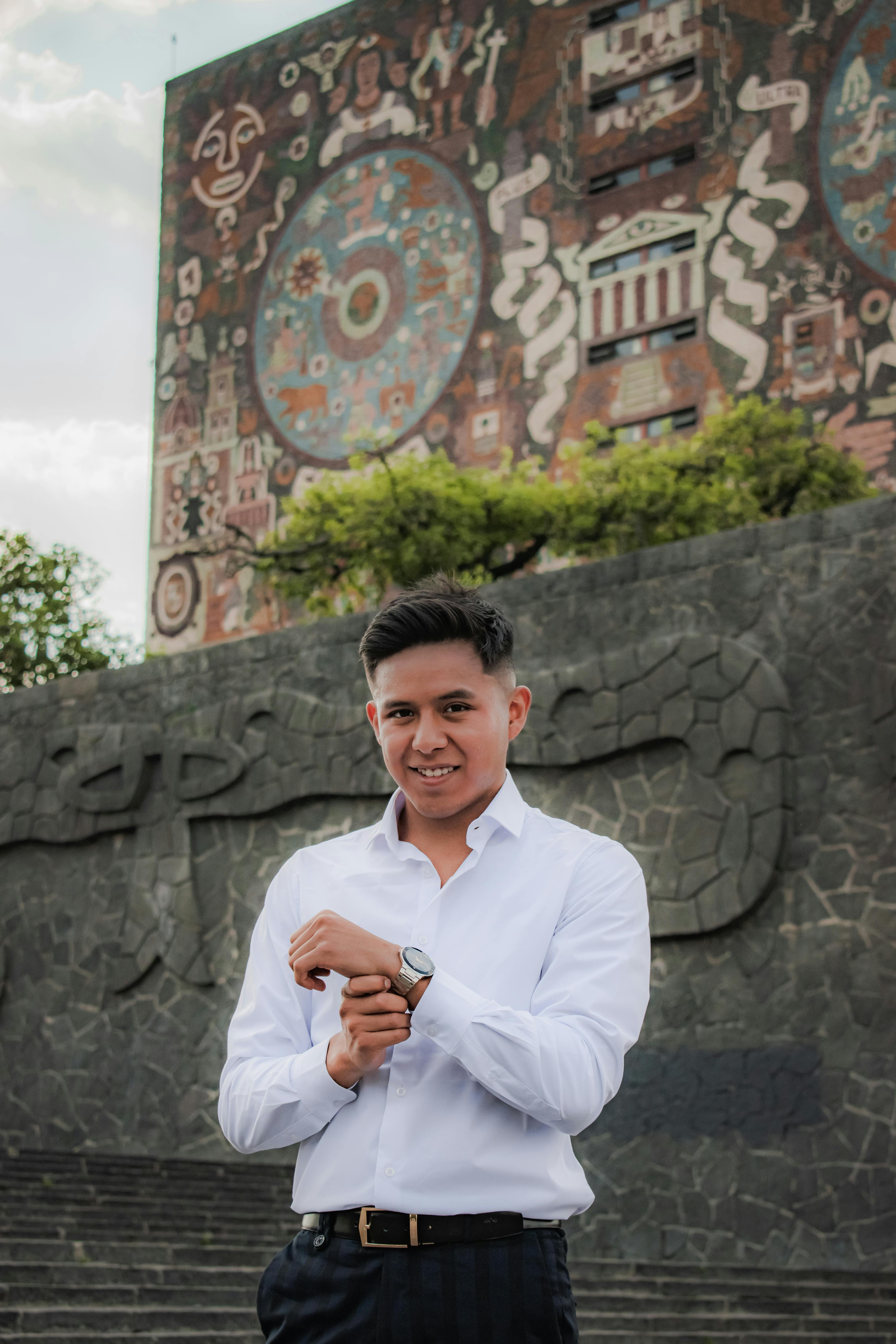 Man in a white shirt stands smiling in front of UNAM Library in Mexico City, showcasing its iconic mural.