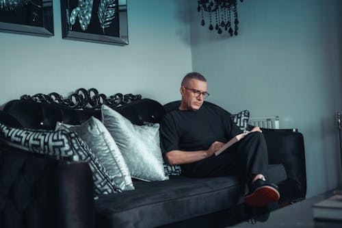 Free Man Sitting on a Sofa and Reading a Book  Stock Photo