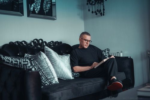 Free Adult man reading on a black couch in a modern living room with decorative cushions. Stock Photo