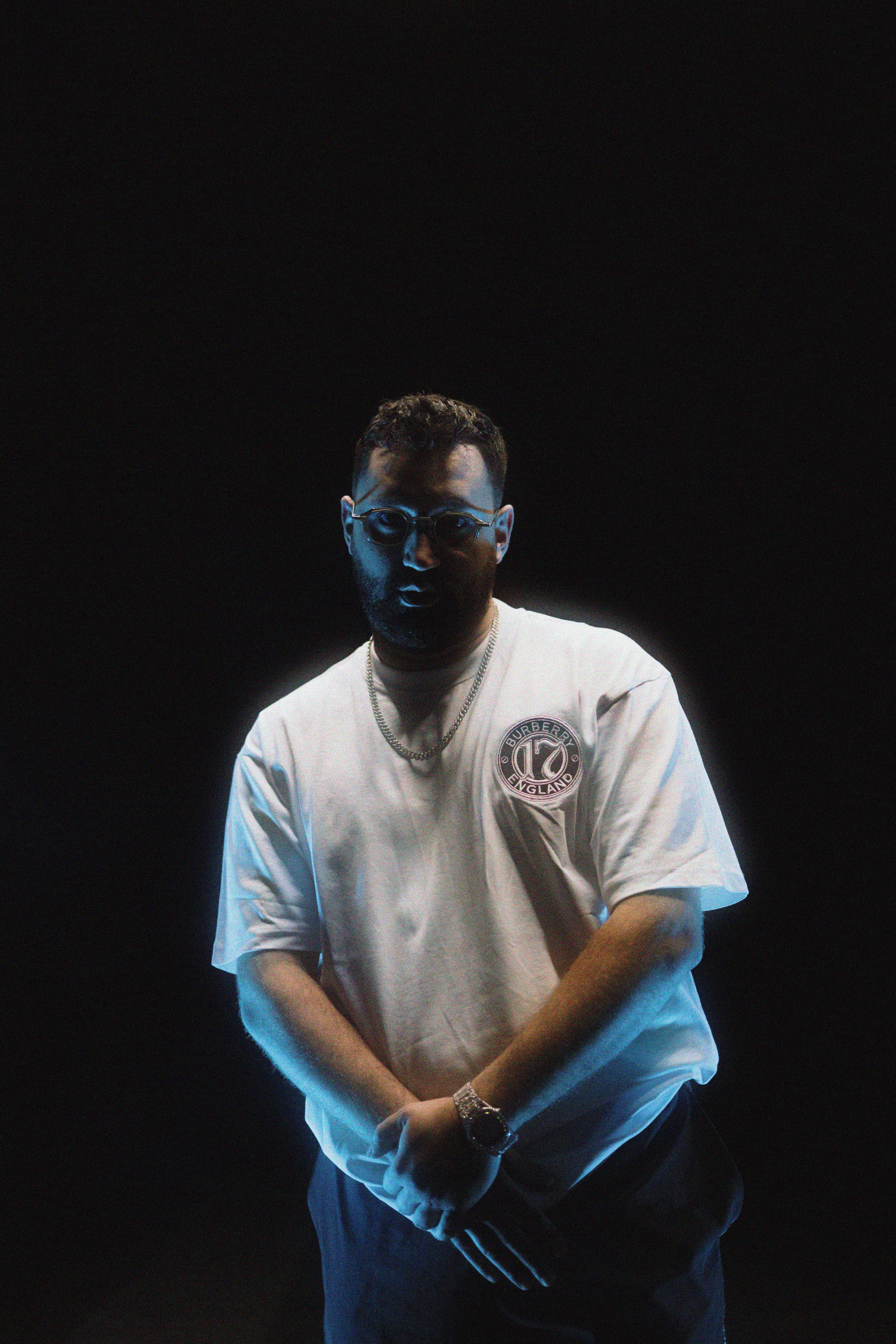 Stylish man wearing eyeglasses poses confidently against a black backdrop in a studio setting.