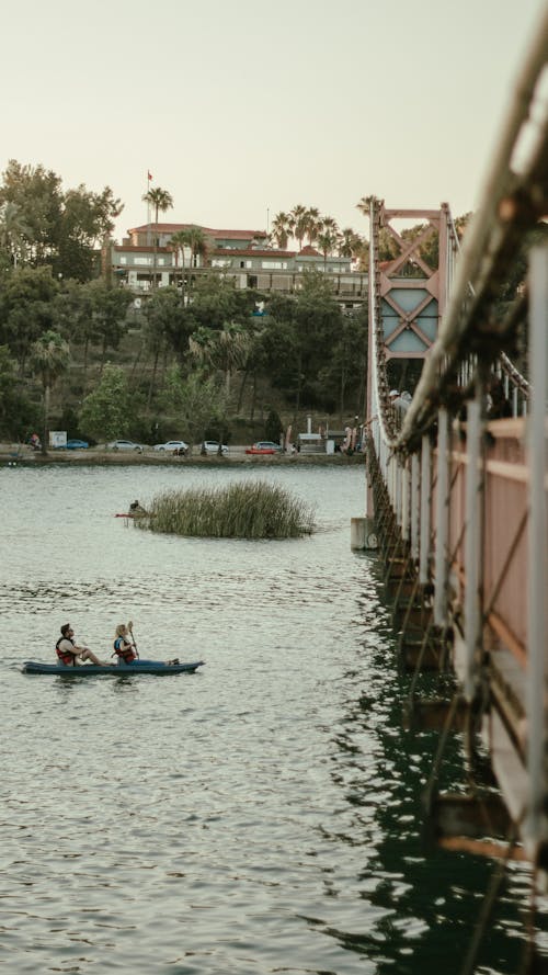 Two People in Canoe Rowing Towards a River Bridge