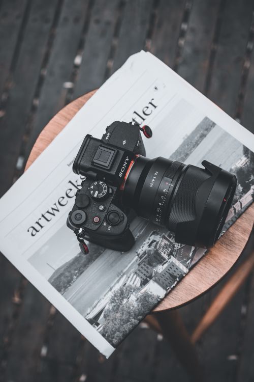 Free Top view of a DSLR camera resting on a newspaper placed on a wooden stool. Stock Photo
