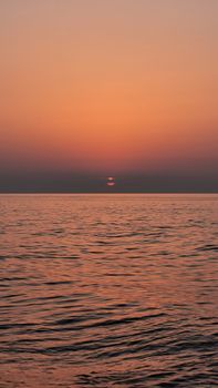 Tranquil ocean scene with a stunning sunset casting pink hues on the sky and water.