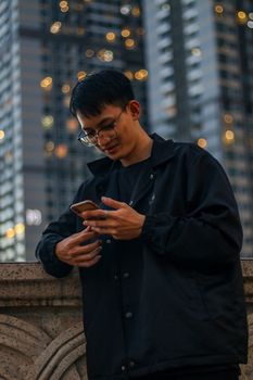 Young man using smartphone in downtown area at night, city lights in backdrop.