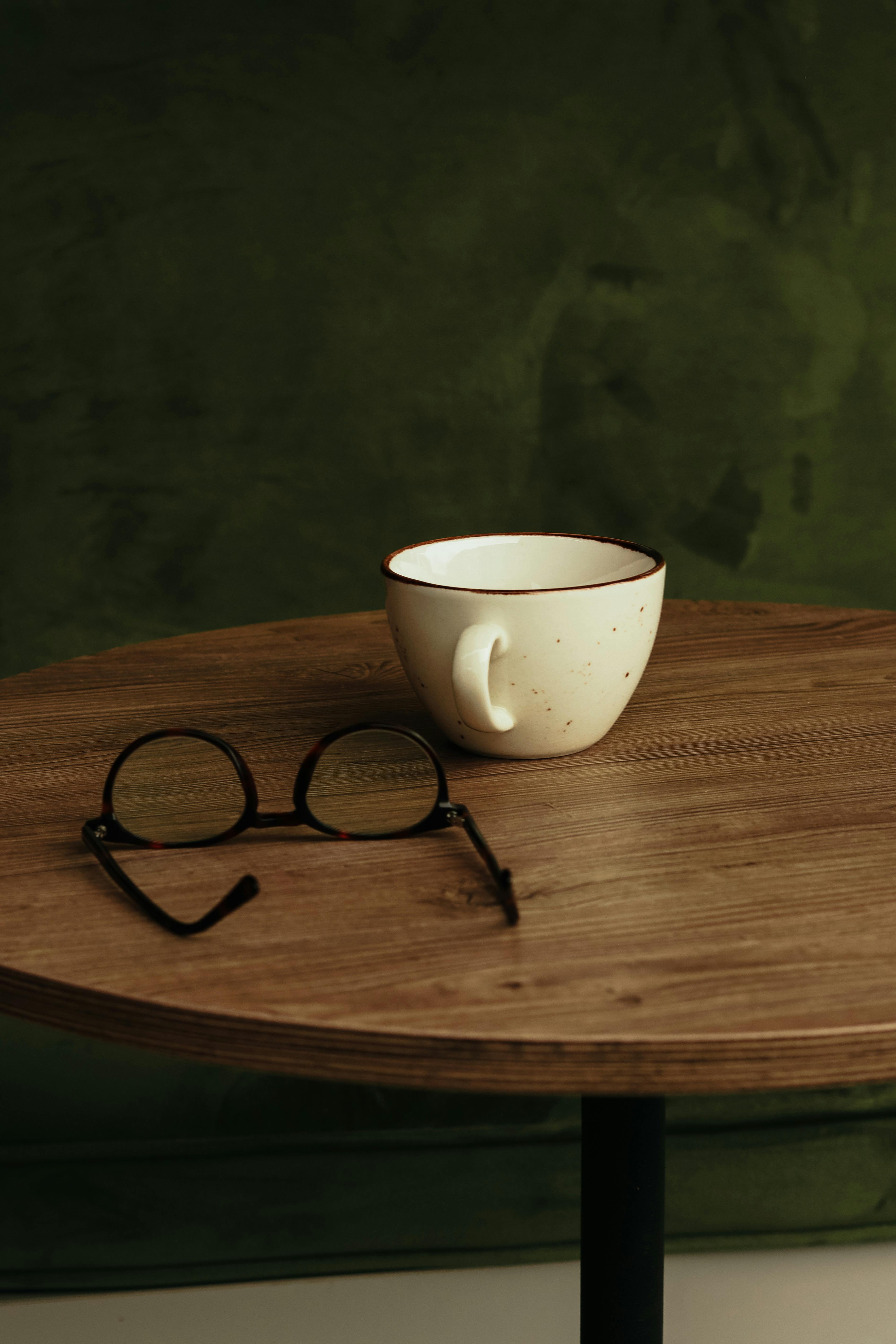 Free Close-up shot of a cup and eyeglasses on a wooden table, perfect for cozy indoor settings. Stock Photo