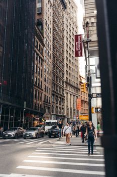 A vibrant city street scene featuring people on a crosswalk surrounded by tall buildings and traffic.