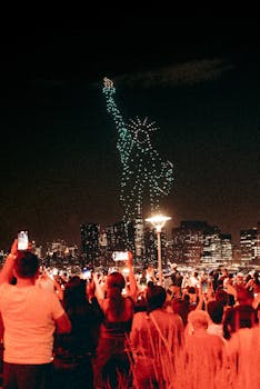 A vibrant drone light show forms the Statue of Liberty as a crowd captures the spectacle at night.