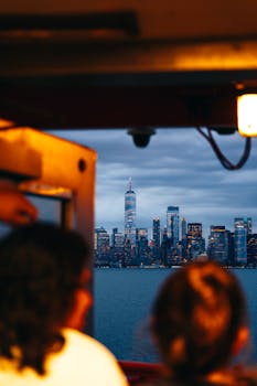 Cityscape of New York City skyline viewed from a boat at twilight with two people in the foreground.