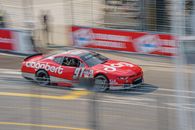 Red race car with bold livery speeding on Toronto circuit track, capturing the thrill of motorsport.