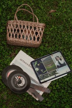 A charming flat lay of a wicker basket, vinyl records, and a tablet on grass.