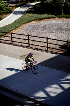 Cyclist riding a road bicycle on a city street, captured from above on a sunny day.