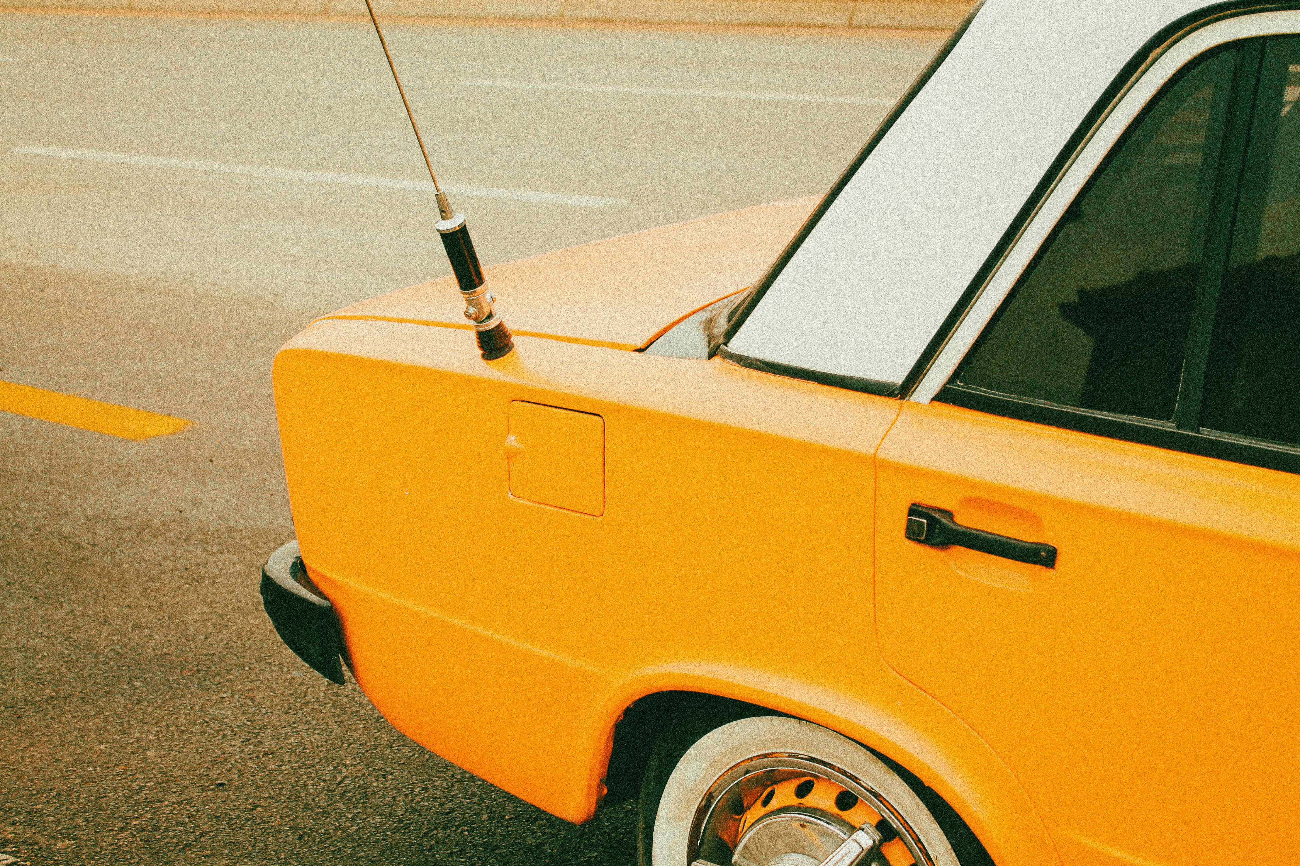 Detailed shot of a yellow vintage car parked on an urban road, highlighting its classic design.
