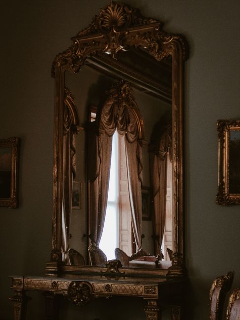A vintage baroque-style mirror reflecting elegant drapery in a classic interior setting.