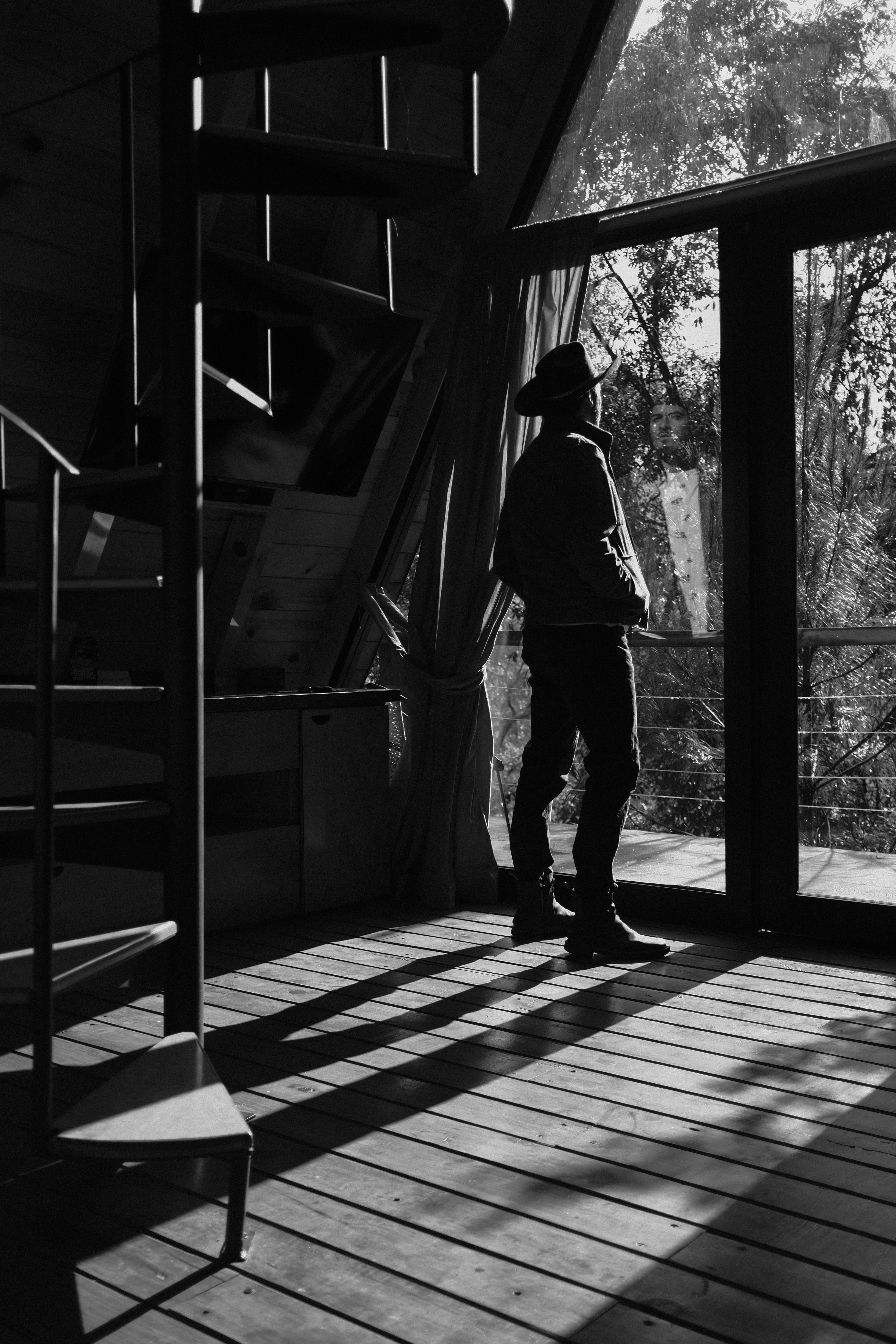 A man in a hat stands silhouetted against large windows, casting shadows indoors.