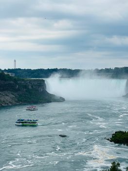 A breathtaking aerial view of Niagara Falls with tour boats on the river below in overcast weather.