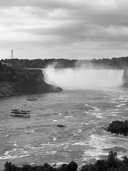 Dramatic black and white photo of Niagara Falls with boats on the river, showcasing natural beauty.