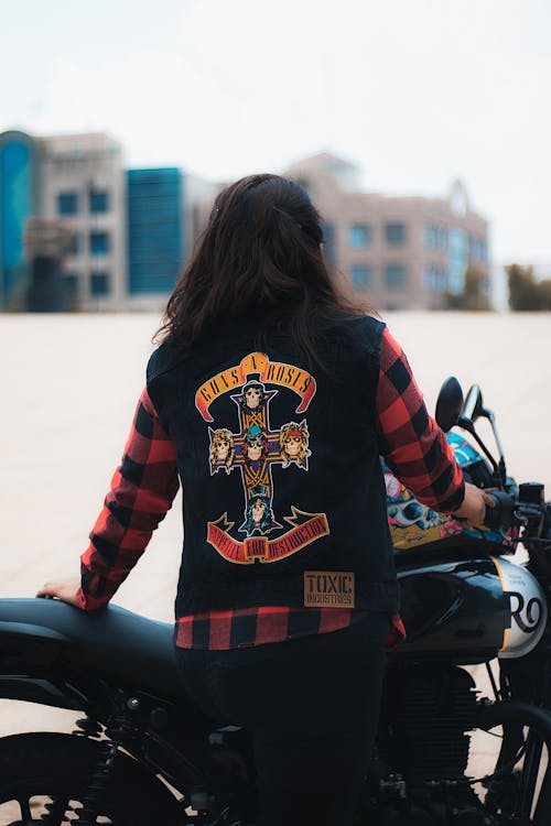 Biker in a Black Denim Vest with a Guns n Roses Print on the Back Posing by the Motorcycle
