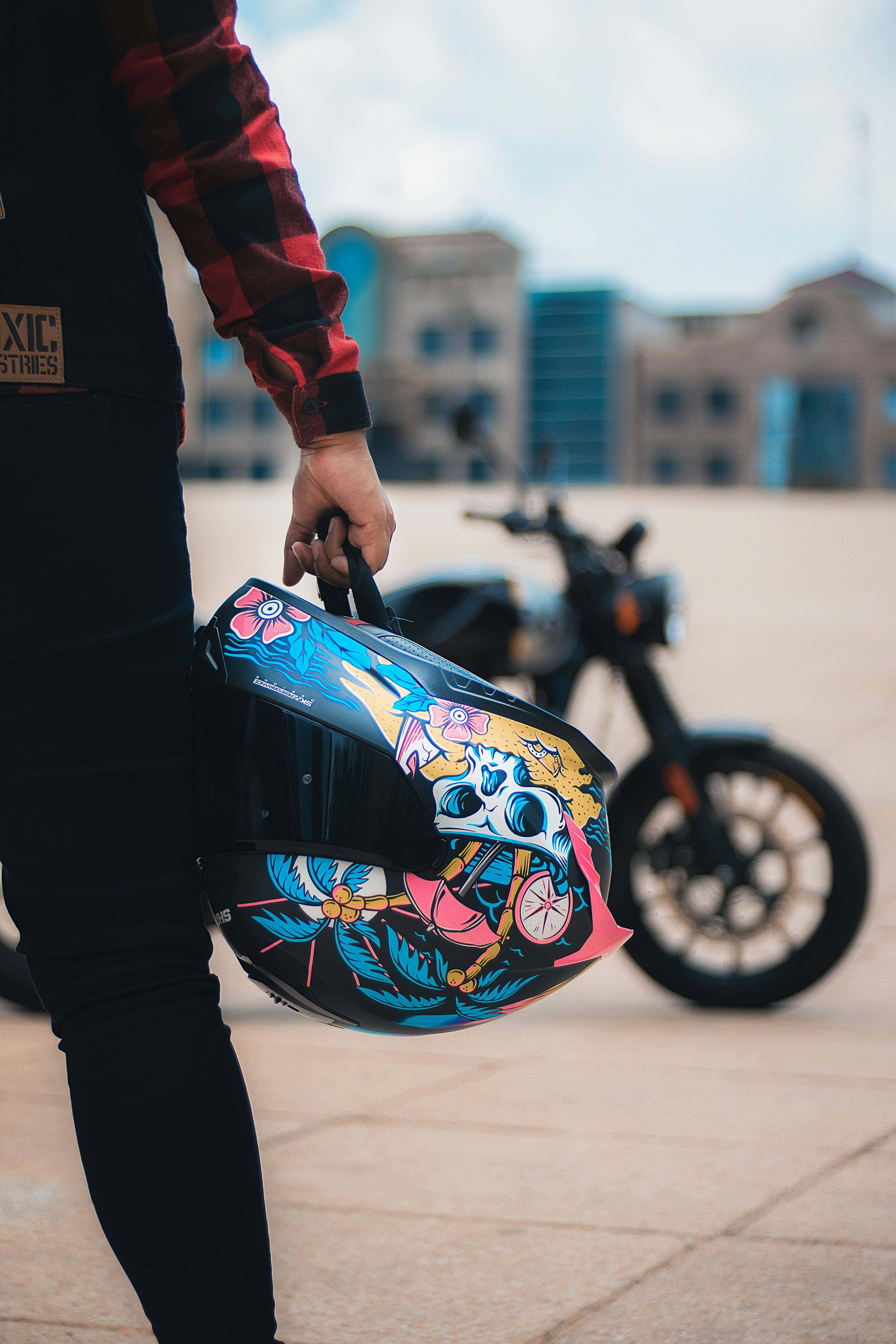 Free Man holding a colorful helmet with a motorcycle in urban setting, selective focus. Stock Photo