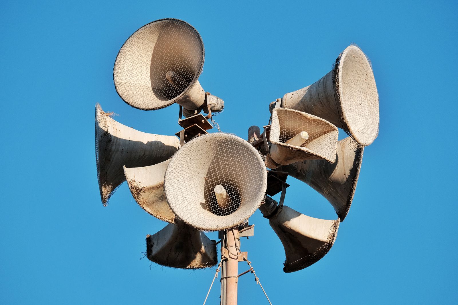 Close-up of weathered megaphones mounted on a pole against blue sky