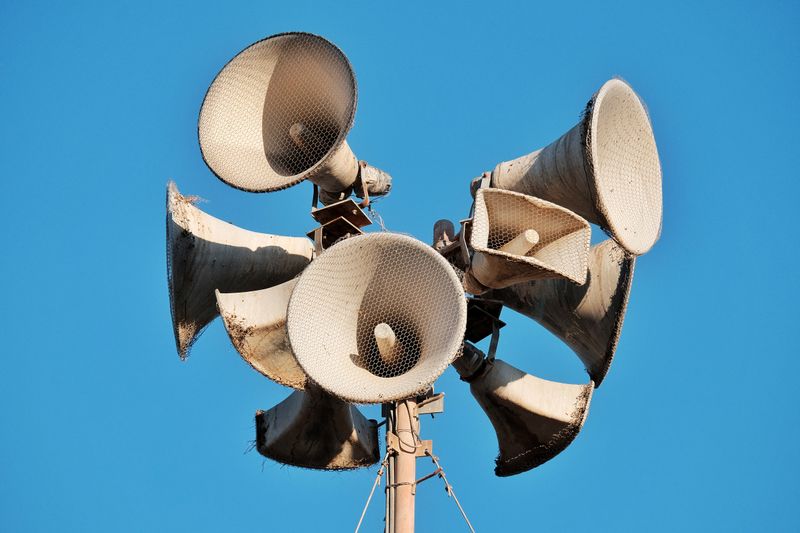 Close-up of weathered megaphones mounted on a pole against blue sky