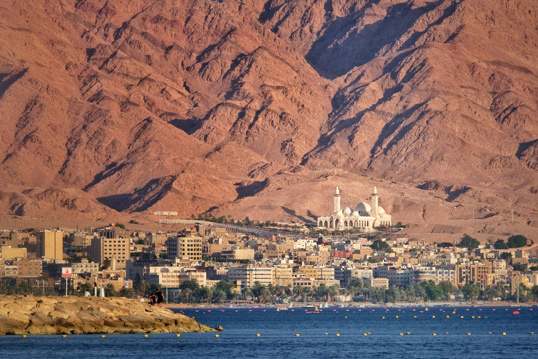 A scenic view of Aqaba city against a dramatic mountain backdrop by the sea.
