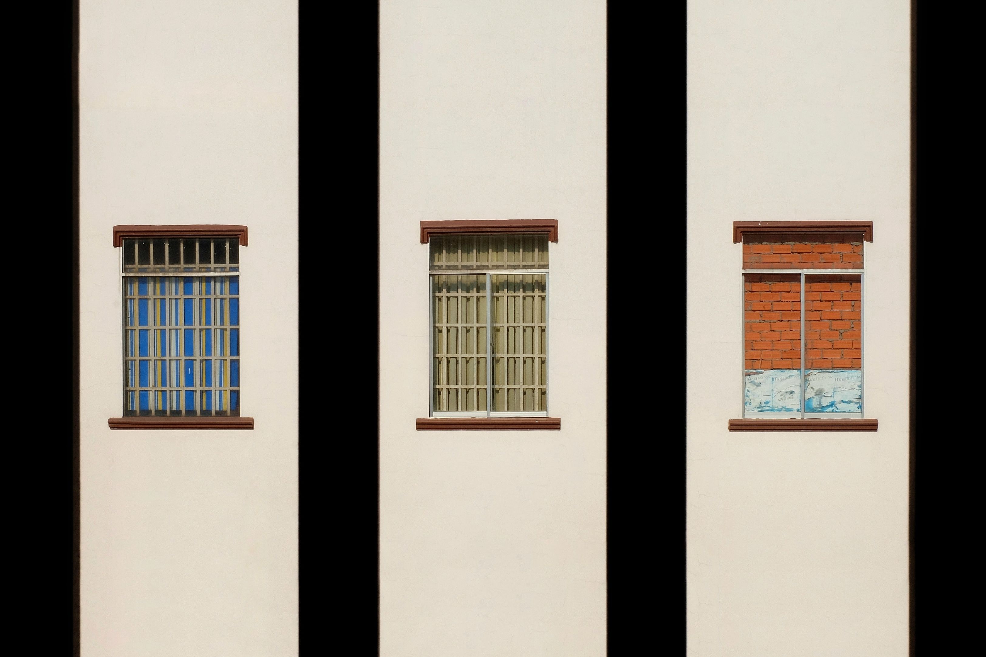 Fotomural Tres ventanas distintas en una pared de edificio de la ciudad iluminada por el sol, mostrando diseños variados.