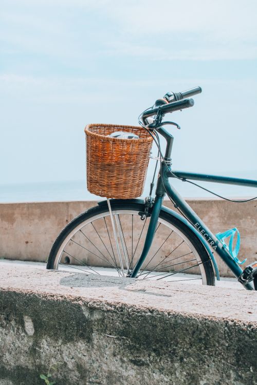 Free A bicycle with a wicker basket stands by the beach, evoking a peaceful summer day. Stock Photo