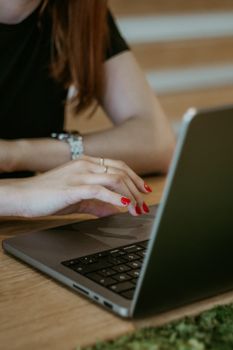 Close-up of a woman typing on a laptop, focusing on her hands in an office environment.